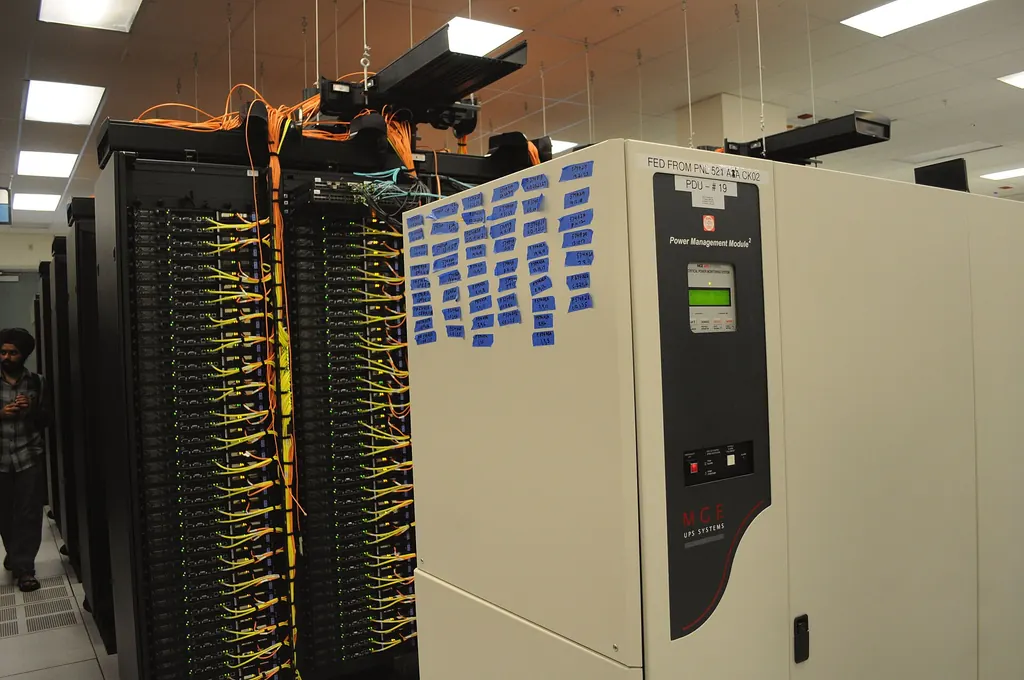 Rows of server racks with yellow and orange network cables running to every unit, next to a power management cabinet