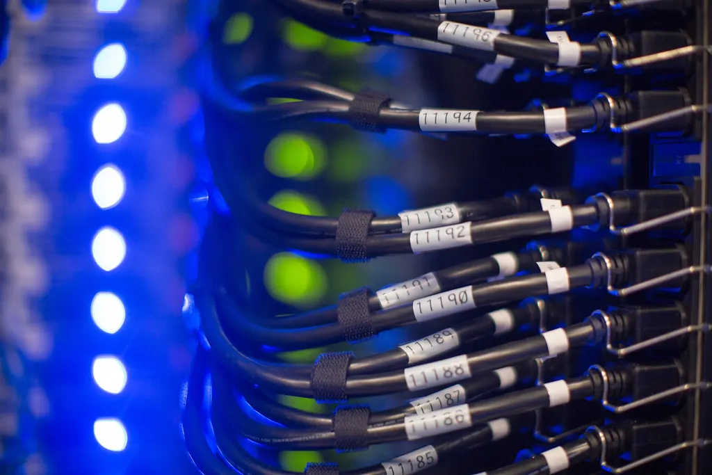 Close-up of numbered, labelled power cables plugged into a server rack under blue light