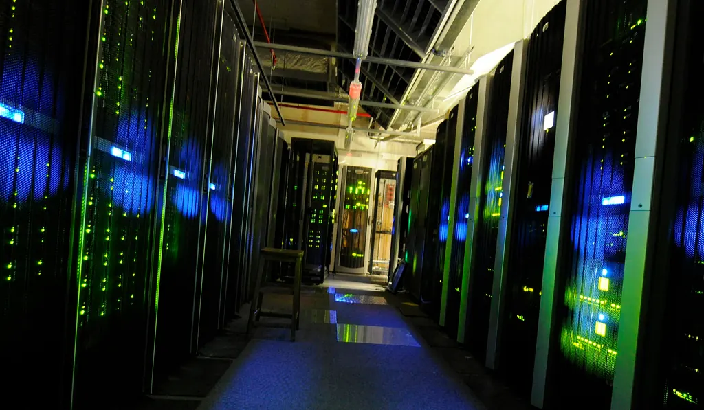 A narrow aisle between rows of server racks with green and blue status lights in a server room