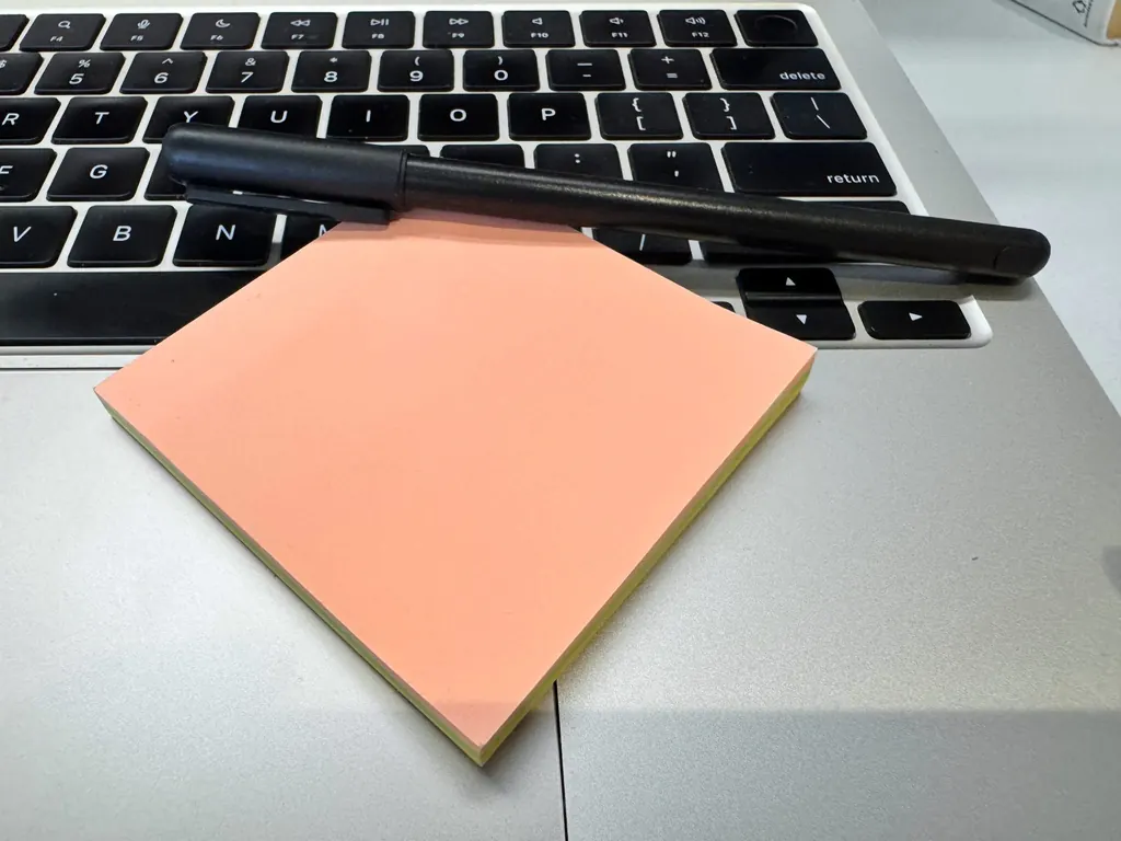 Pad of peach sticky notes and a black pen resting on a laptop keyboard