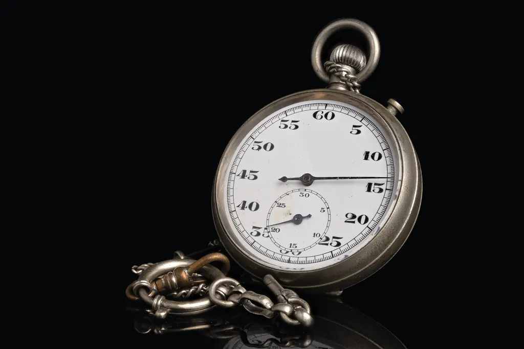 A vintage silver stopwatch with a white dial on a black reflective surface