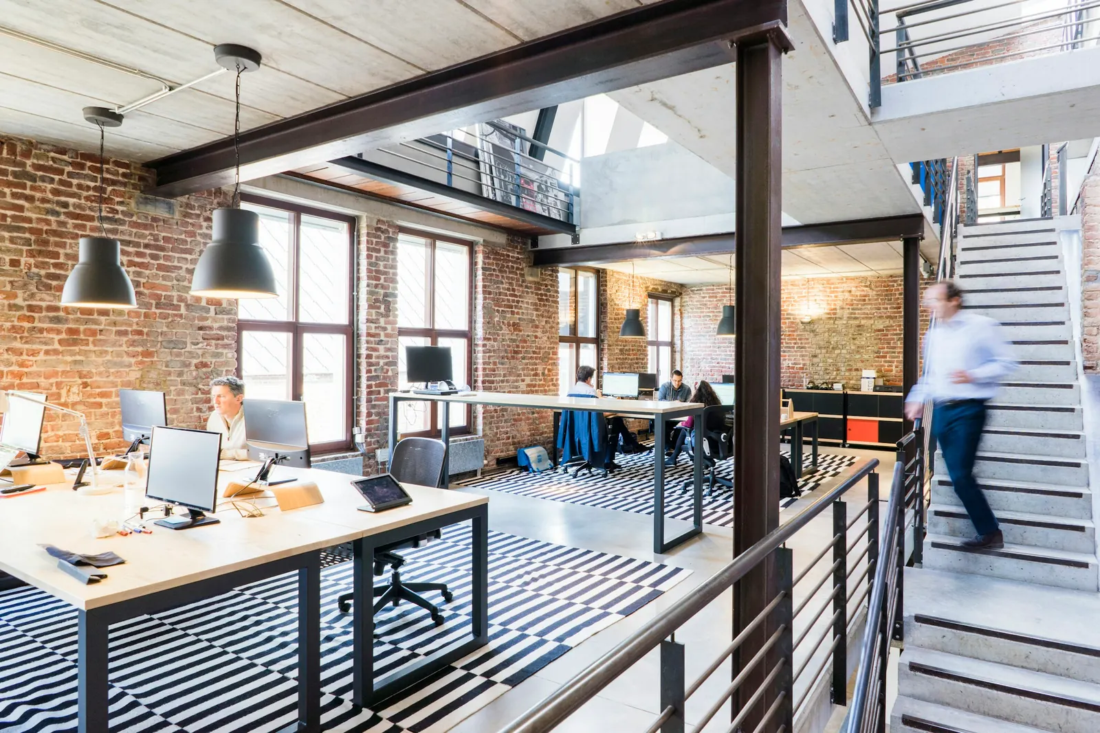 Open-plan loft office with desks, brick walls and a staircase